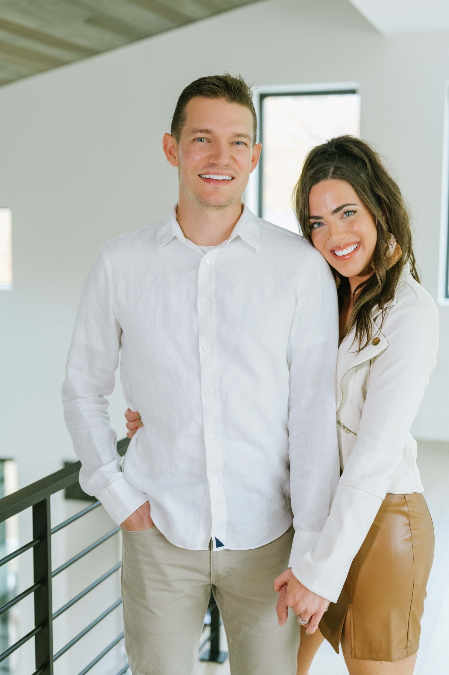 Smiling couple holding hands indoors, dressed in white shirts, exuding a relaxed and happy demeanor.